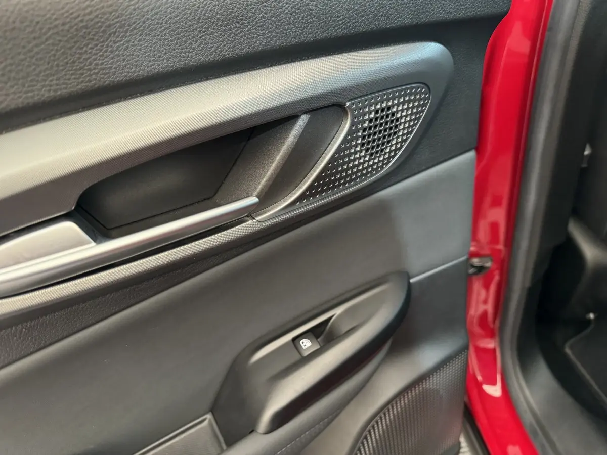 Gros plan sur la porte intérieure côté gauche de l'Alfa Romeo Tonale rouge, avec poignée alu et commande de vitre.