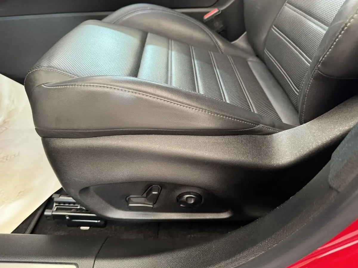 Gros plan sur le siège conducteur noir en cuir perforé de l'Alfa Romeo Tonale rouge, montrant les commandes électriques.