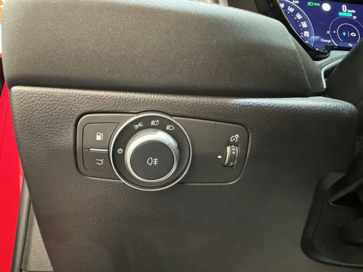 Gros plan sur la commande des phares et éclairage intérieur noir dans l'Alfa Romeo Tonale rouge, côté gauche du tableau de bord.