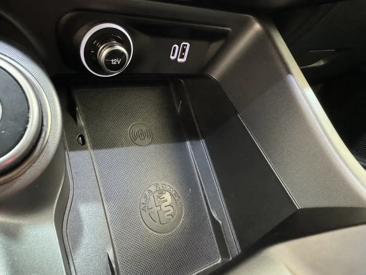 Gros plan sur la console centrale noire de l'Alfa Romeo Tonale avec logo, prise 12V et port USB visible.