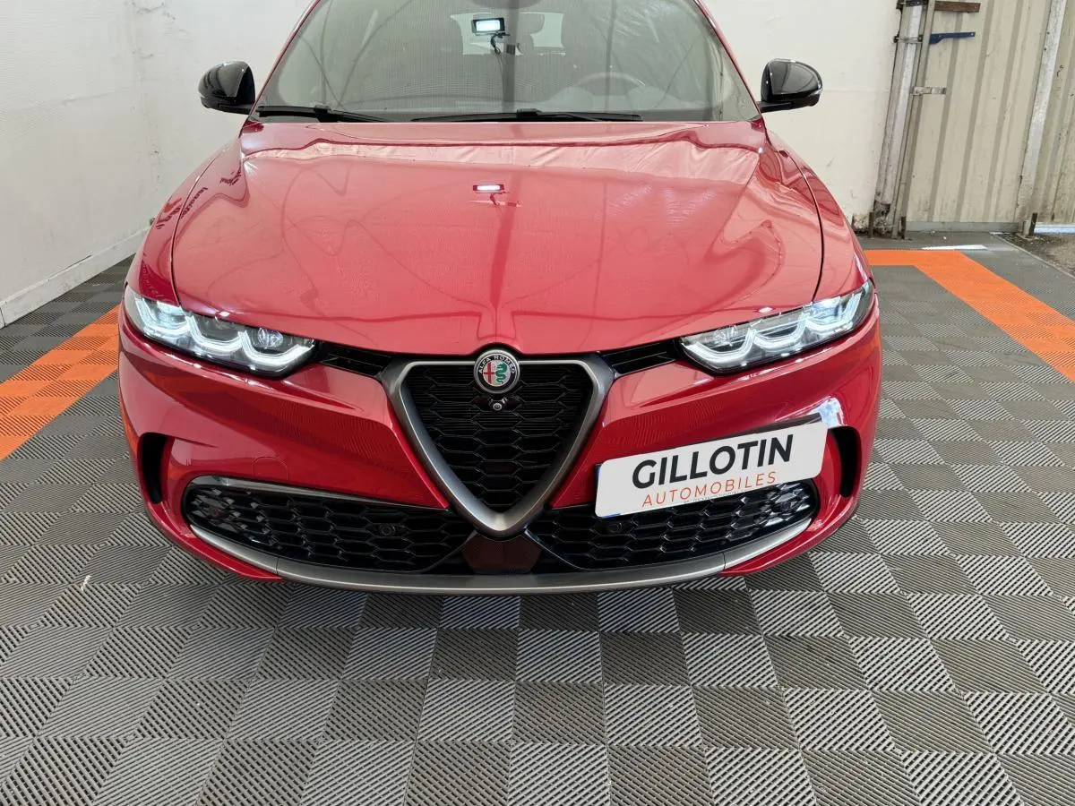 Vue frontale d'une Alfa Romeo Tonale rouge avec calandre emblématique et phares LED allumés dans un garage.