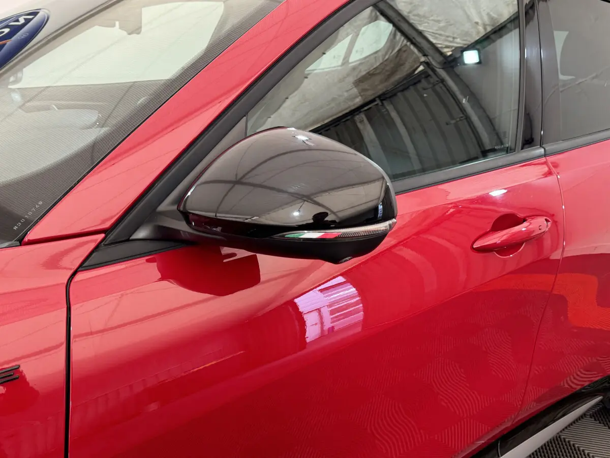 Gros plan sur la porte côté gauche rouge vif de l'Alfa Romeo Tonale avec rétroviseur noir brillant et poignée intégrée.