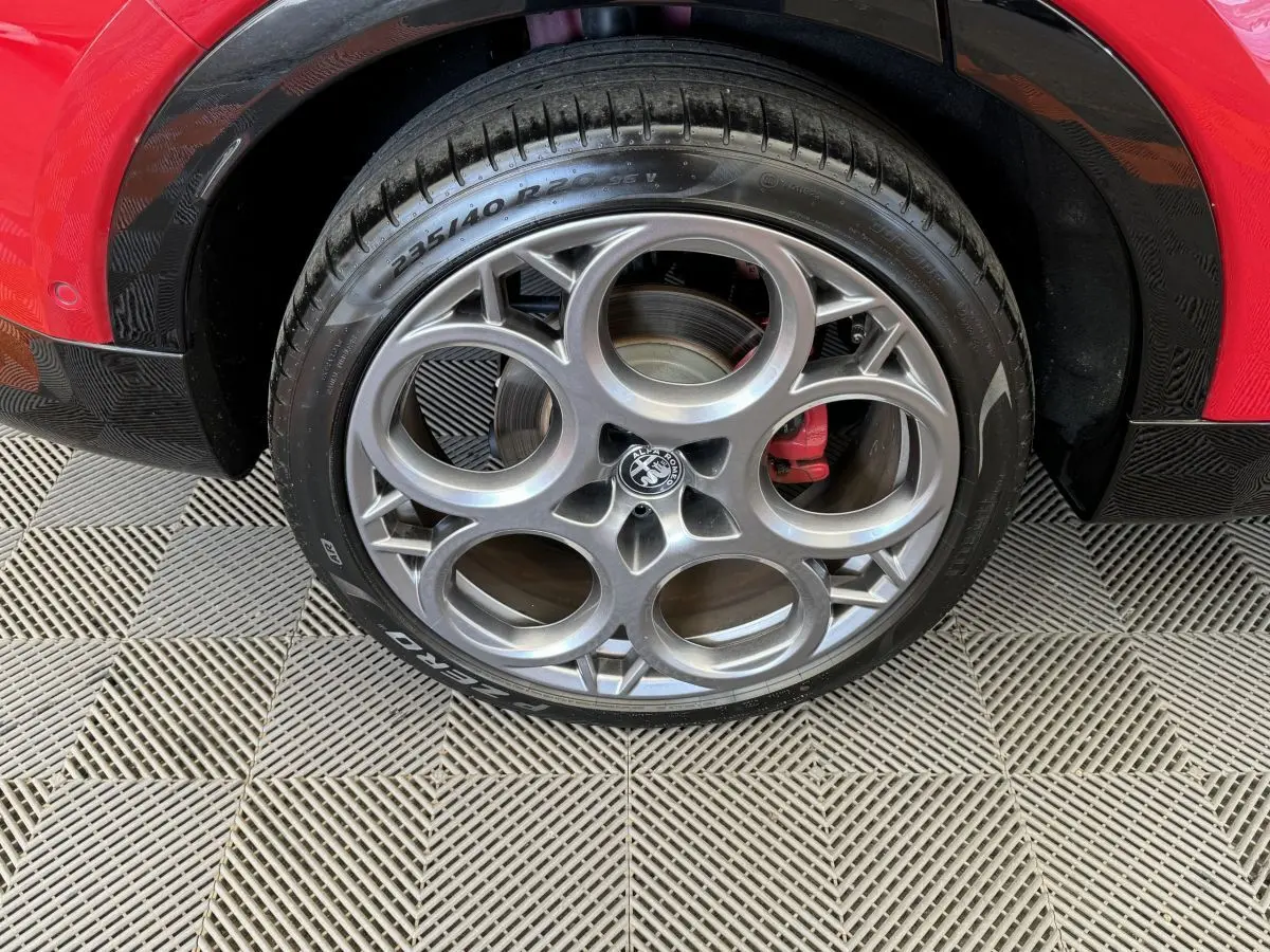Gros plan sur la roue avant droite d'une Alfa Romeo Tonale rouge avec jante alu à cercles entrelacés et étrier de frein rouge.