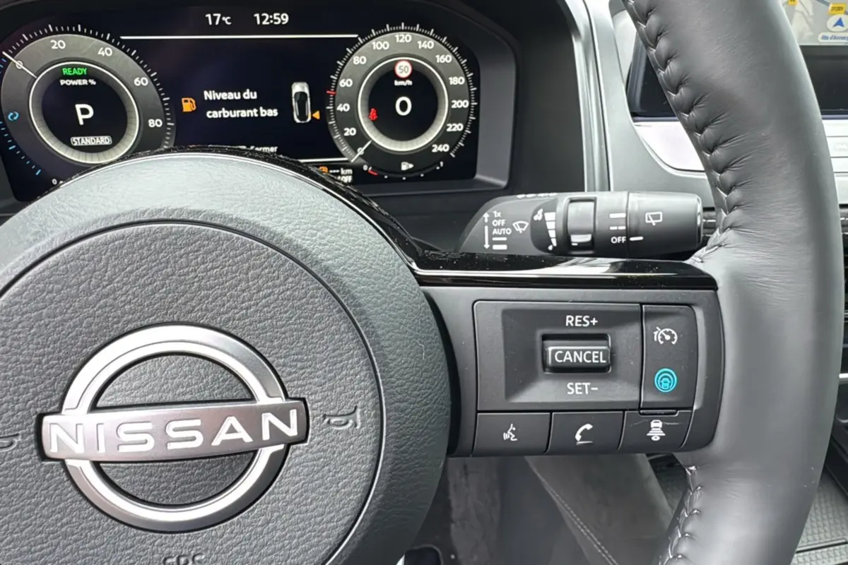 Vue rapprochée du volant cuir multifonctions Nissan Qashqai E-POWER 205 Tekna Plus avec tableau de bord numérique allumé.