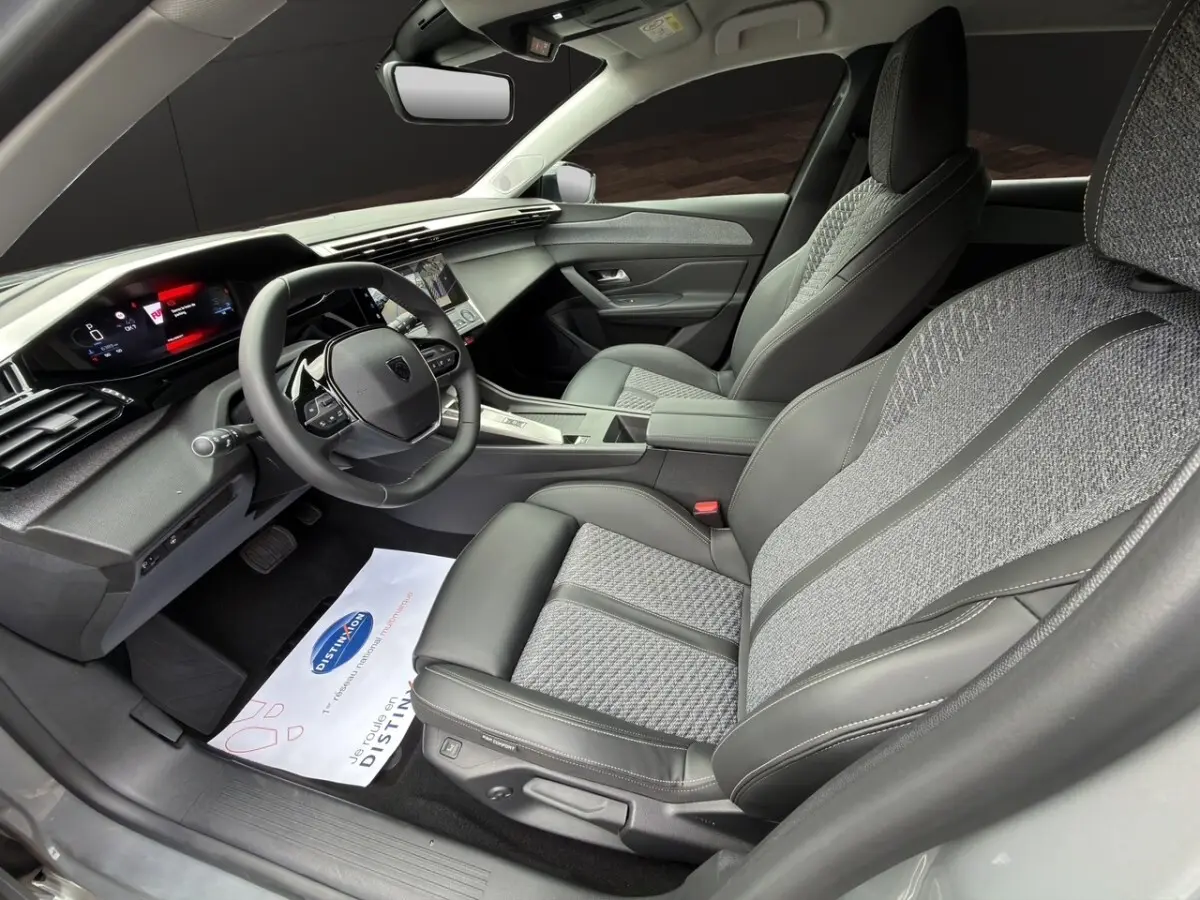 Intérieur de la Peugeot 308 Hybrid 145 e-DCS6 Allure, vue côté conducteur, sièges gris tissu et cuir, tableau de bord moderne.