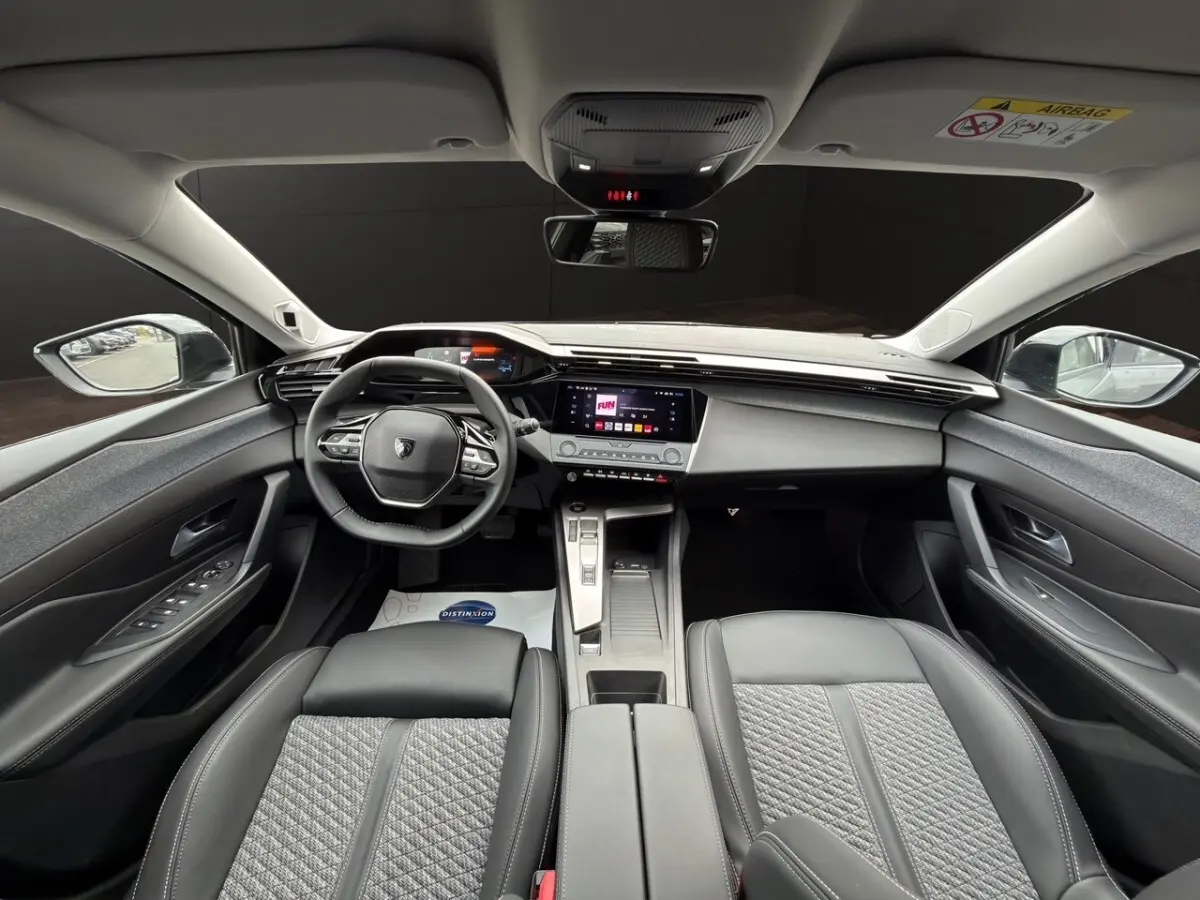 Vue intérieure avant de la Peugeot 308 Hybrid 145 Allure 2025, avec tableau de bord moderne et sièges gris foncé en tissu et cuir.