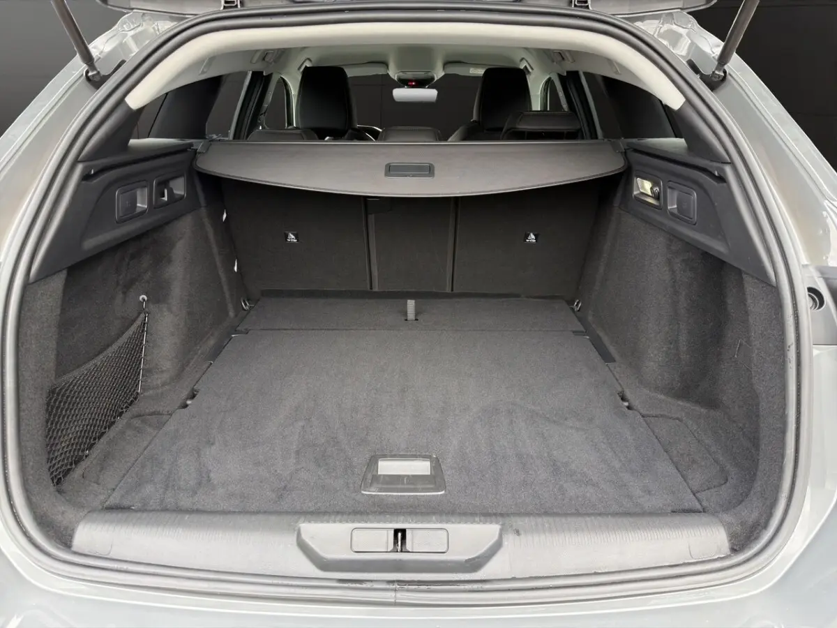 Coffre ouvert vu de l'arrière d'une Peugeot 308 Hybrid 145 gris foncé avec plancher plat et cache-bagages.