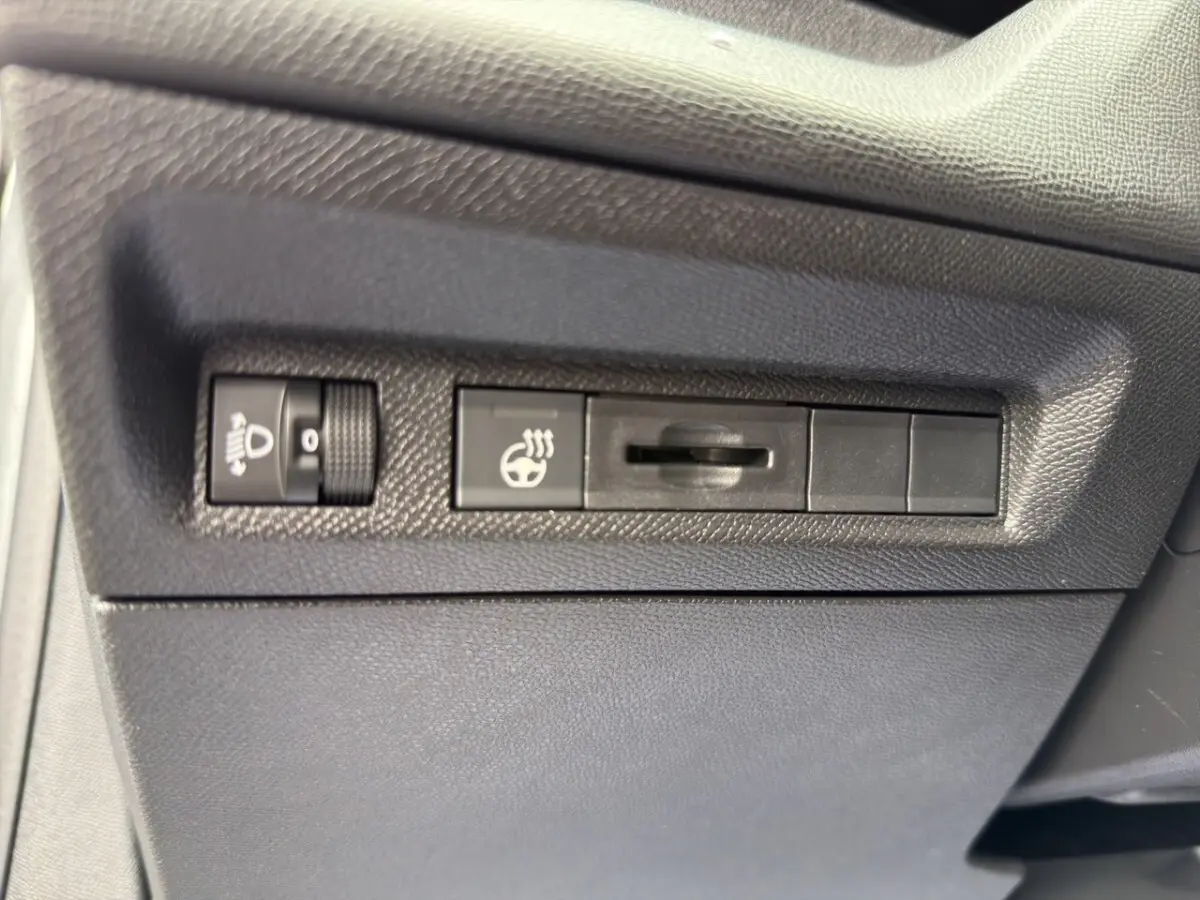 Gros plan sur les commandes de réglage des phares et du volant chauffant dans une Peugeot 308 Hybrid 145 e-DCS6 Allure.