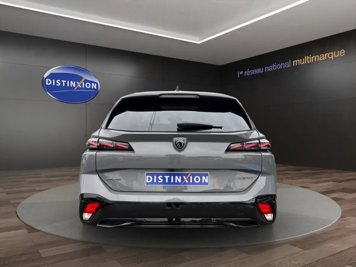 Vue arrière d'une Peugeot 308 Hybrid gris foncé avec feux LED et logo distinctif sur fond noir en showroom.