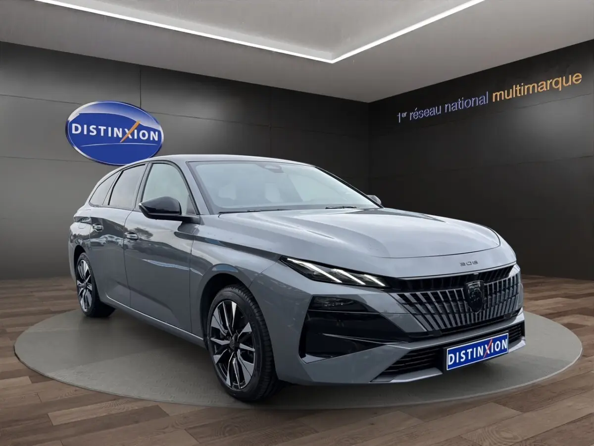 Peugeot 308 Hybrid gris foncé vue 3/4 avant droit, avec calandre noire et phares LED fins en showroom.