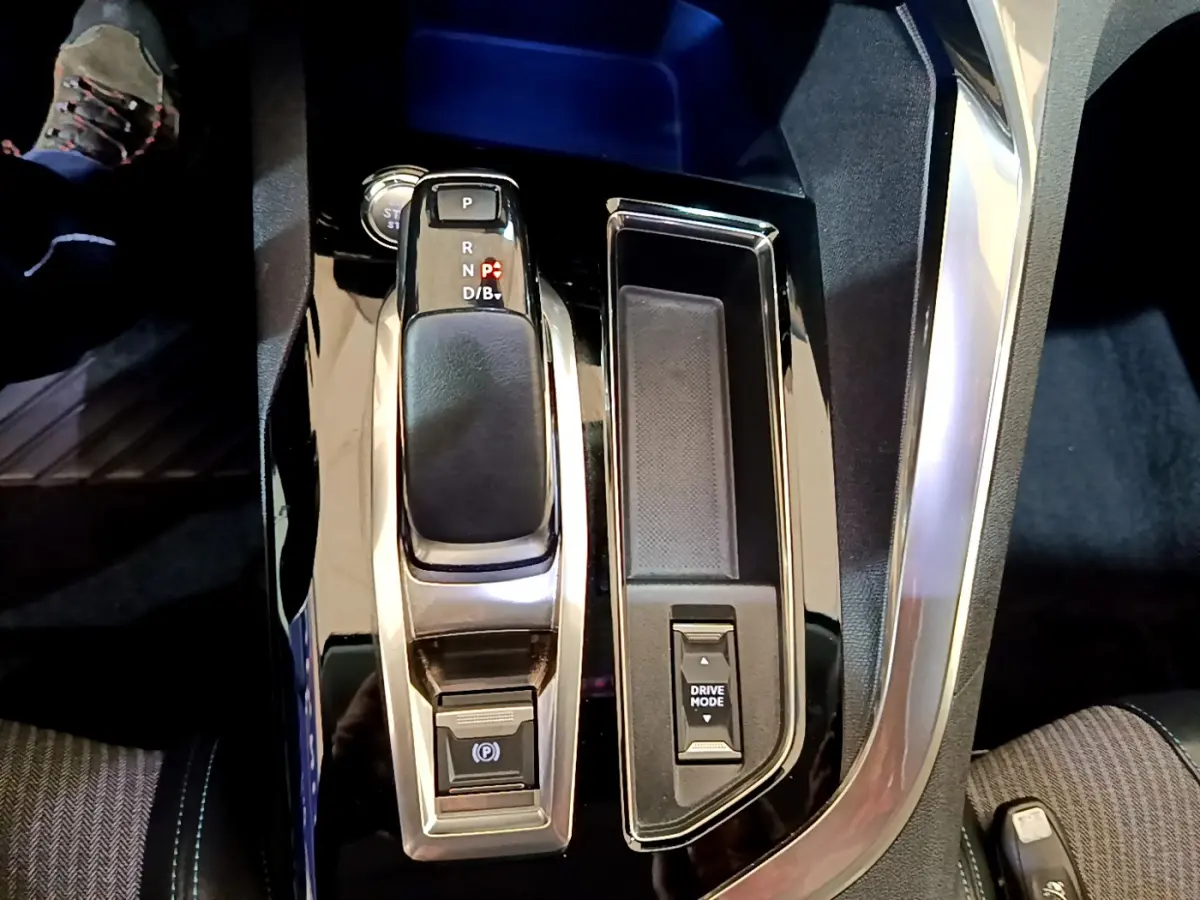 Vue rapprochée de la console centrale noire brillante du Peugeot 3008 bleu, avec levier de vitesse automatique et bouton Drive Mode.