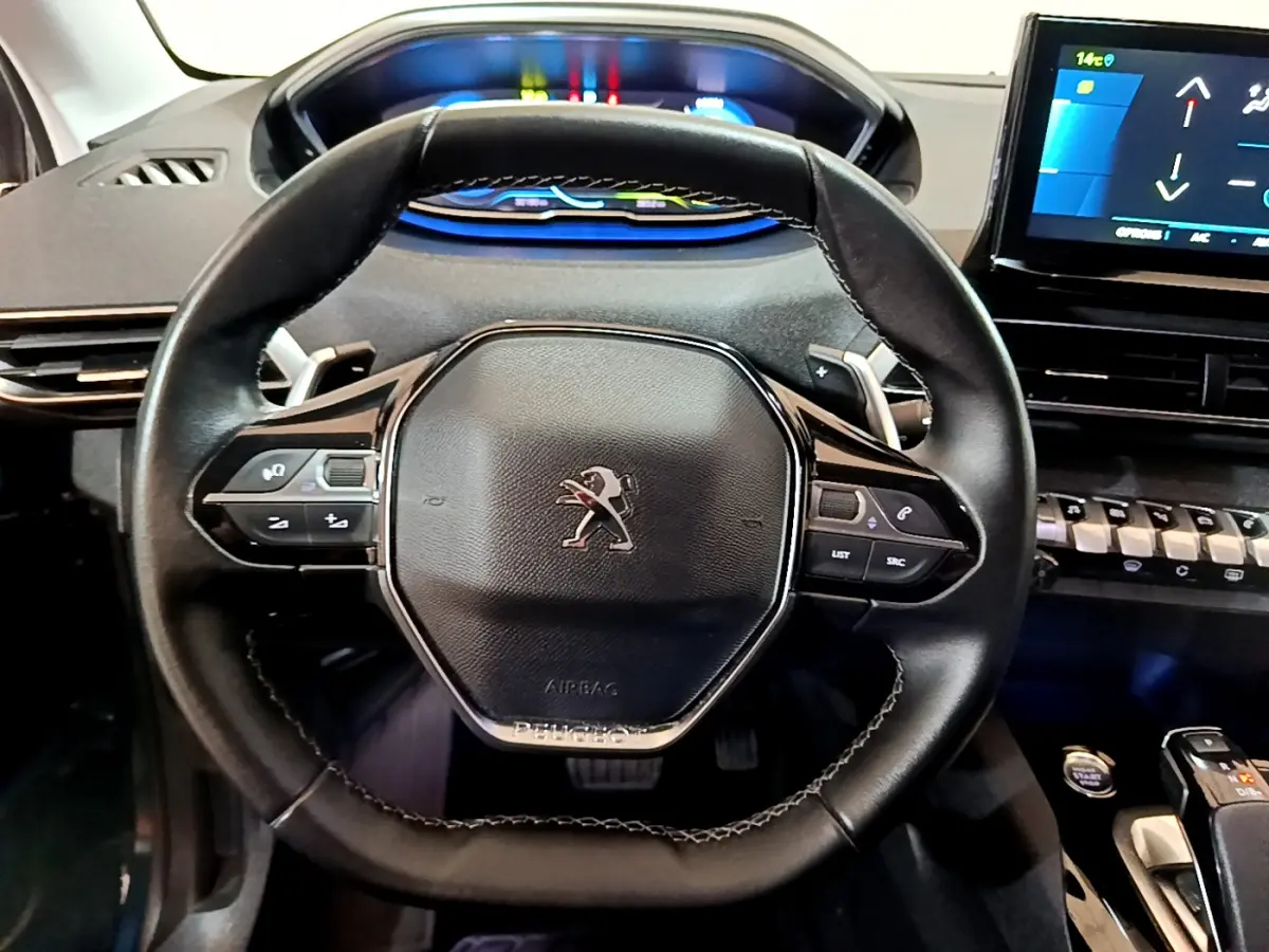 Vue rapprochée du volant cuir noir du Peugeot 3008 hybride 2021 avec tableau de bord digital et écran tactile.