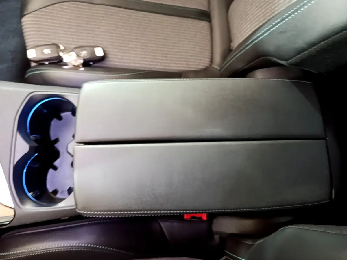 Gros plan sur l'accoudoir central en cuir noir avec surpiqûres bleues et porte-gobelets éclairés d'un Peugeot 3008 hybride bleu.