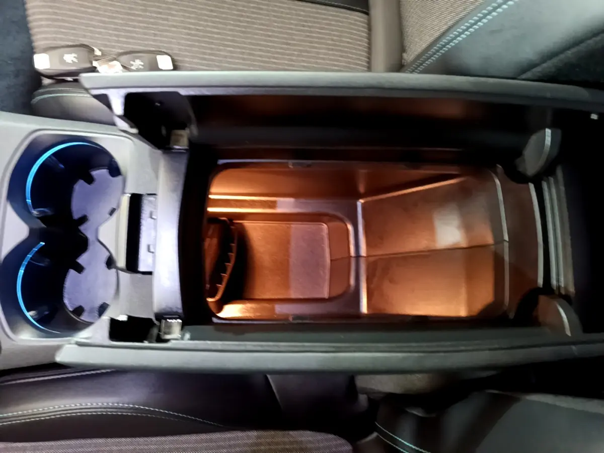 Vue plongeante sur le rangement central éclairé et les porte-gobelets bleutés du Peugeot 3008 hybride rechargeable bleu.