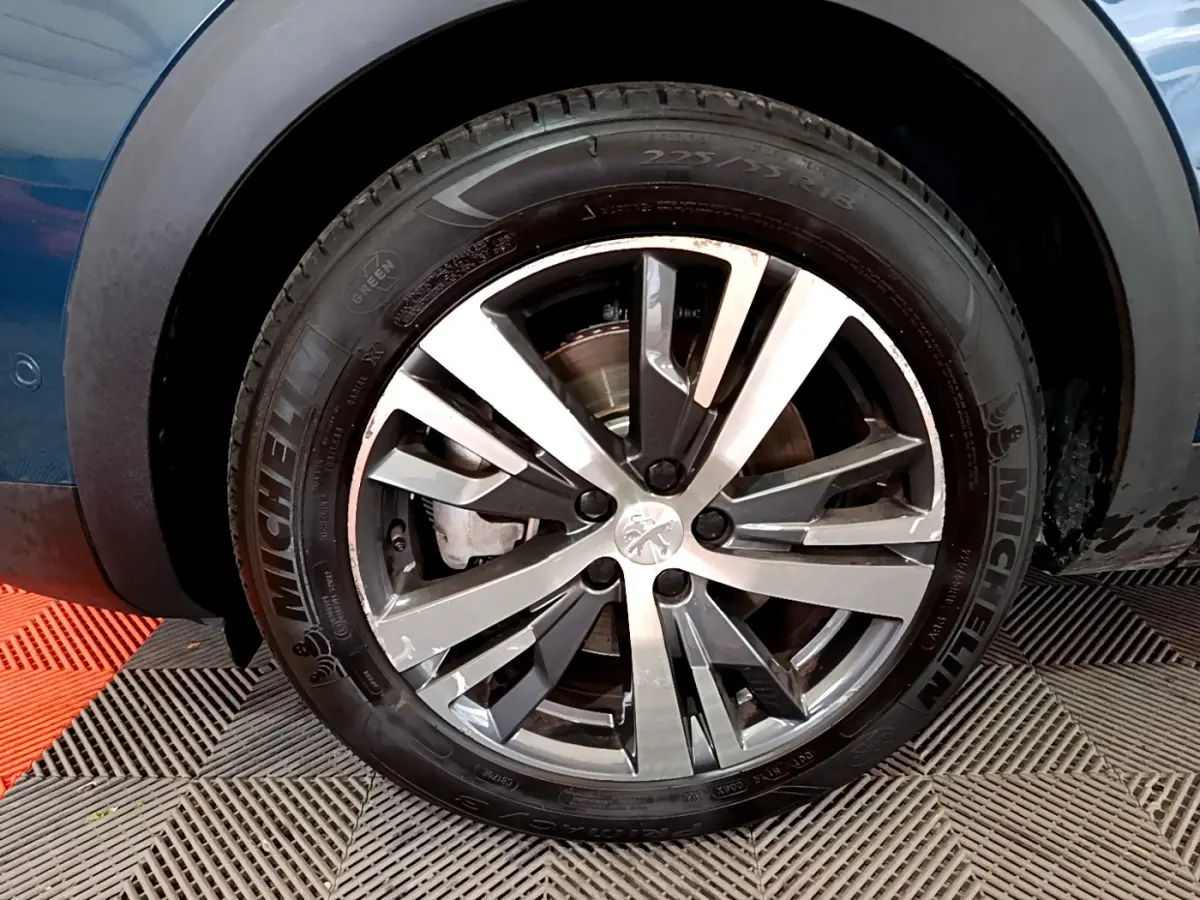 Gros plan sur la roue avant gauche d’un Peugeot 3008 bleu, avec jante alliage et pneu Michelin visible.