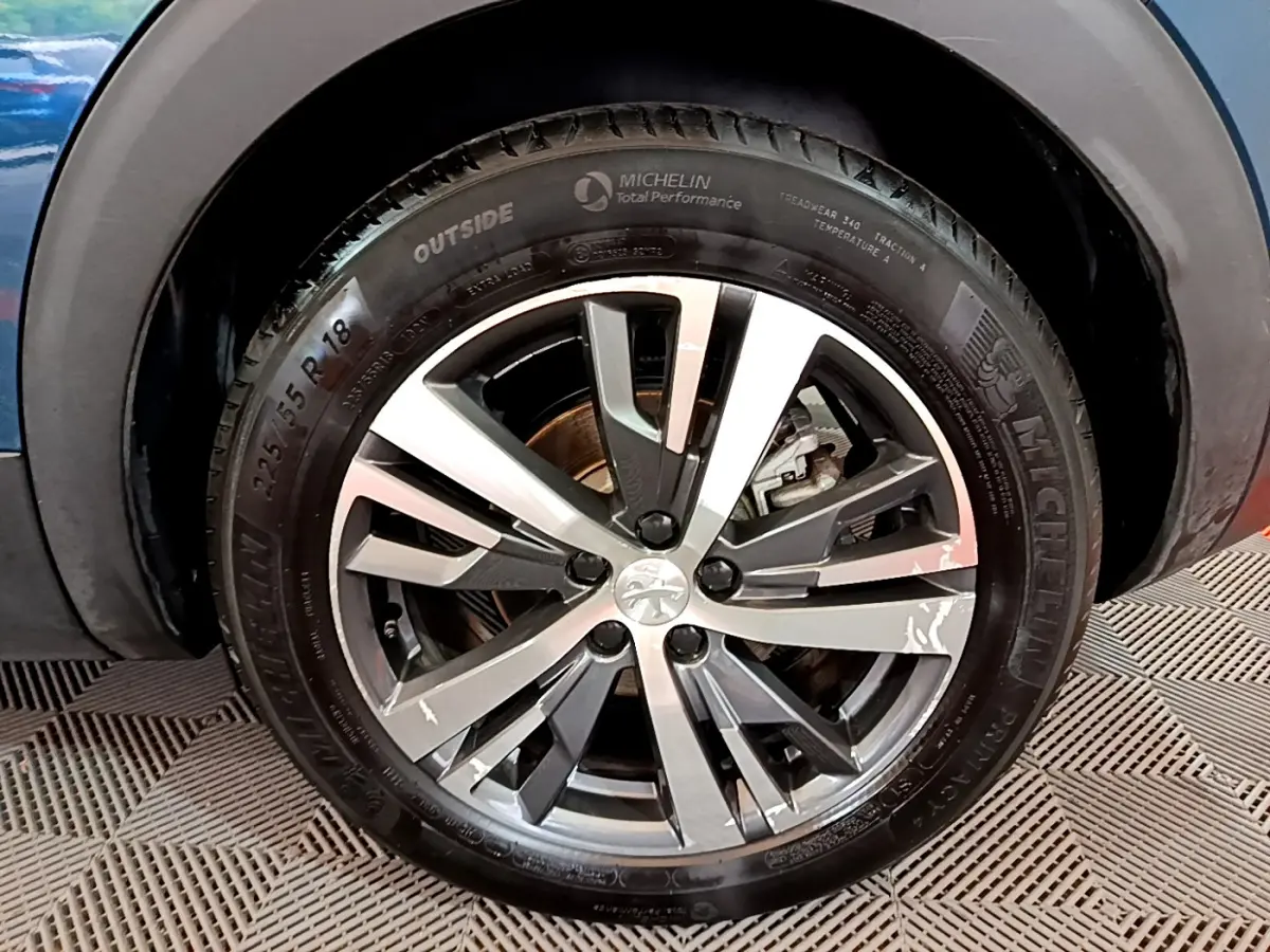 Gros plan sur la roue avant gauche du Peugeot 3008 bleu hybride, jante alliage à design moderne et pneus Michelin.