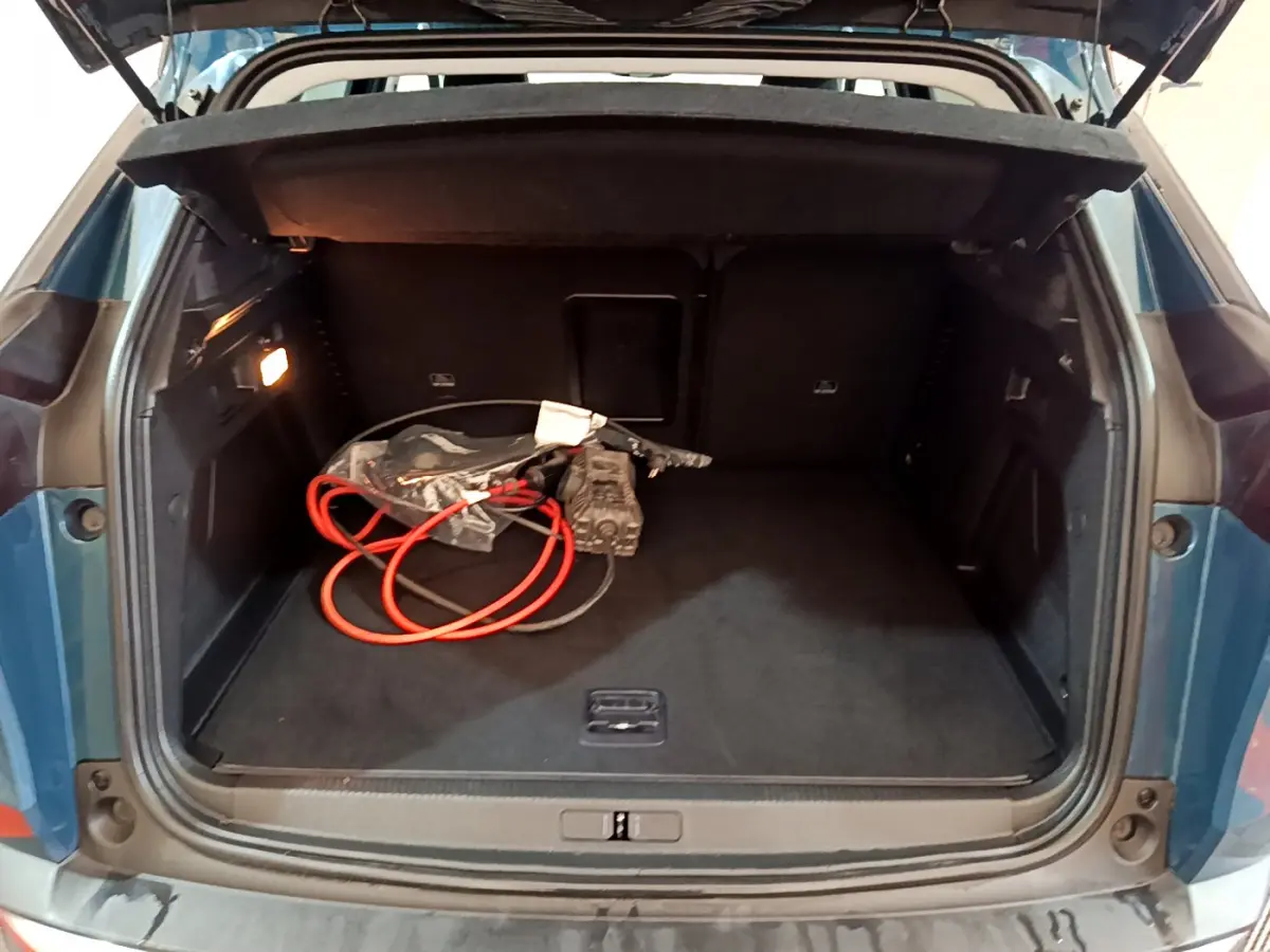 Coffre ouvert d'un Peugeot 3008 bleu hybride rechargeable, vue arrière montrant un câble de charge orange à l'intérieur.