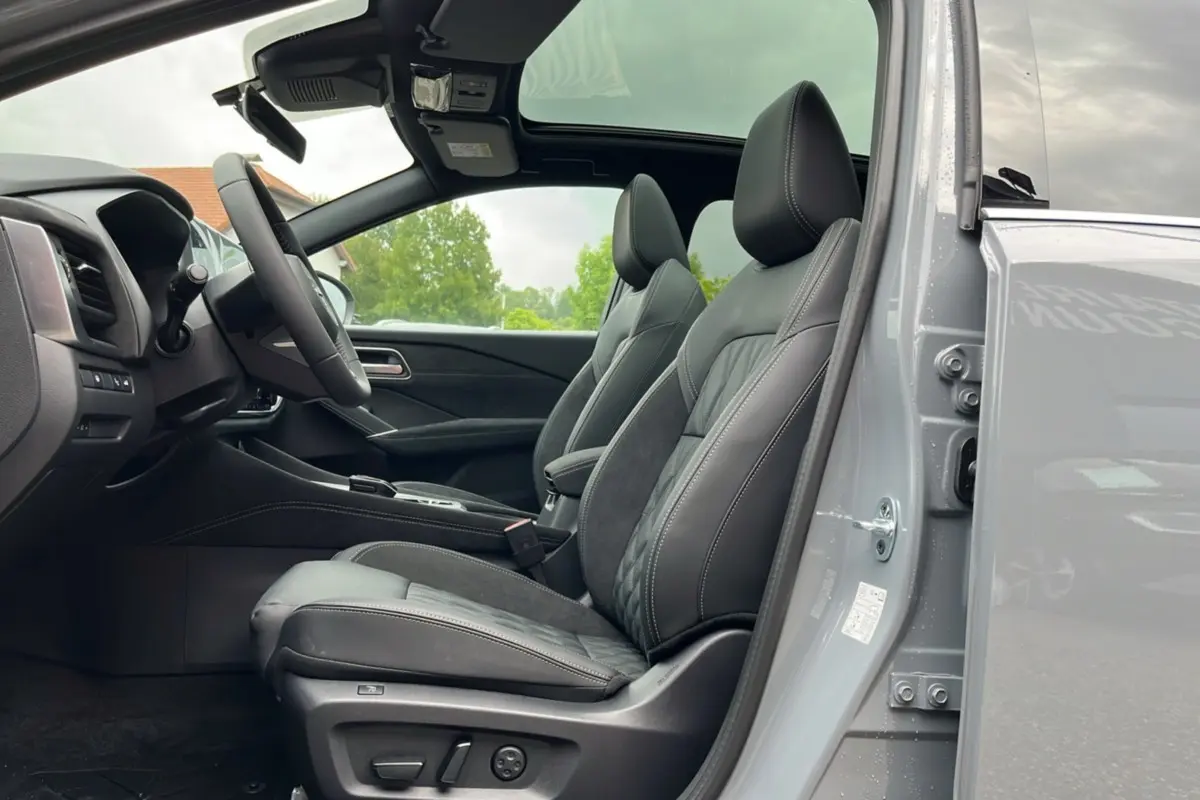 Vue intérieure côté conducteur du Nissan Qashqai E-POWER 205 Tekna Plus gris argile avec sièges cuir et toit panoramique ouvert.