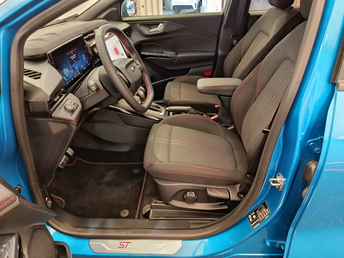 Intérieur côté conducteur du Ford Puma bleu 2025, sièges noirs avec surpiqûres rouges et tableau de bord numérique.