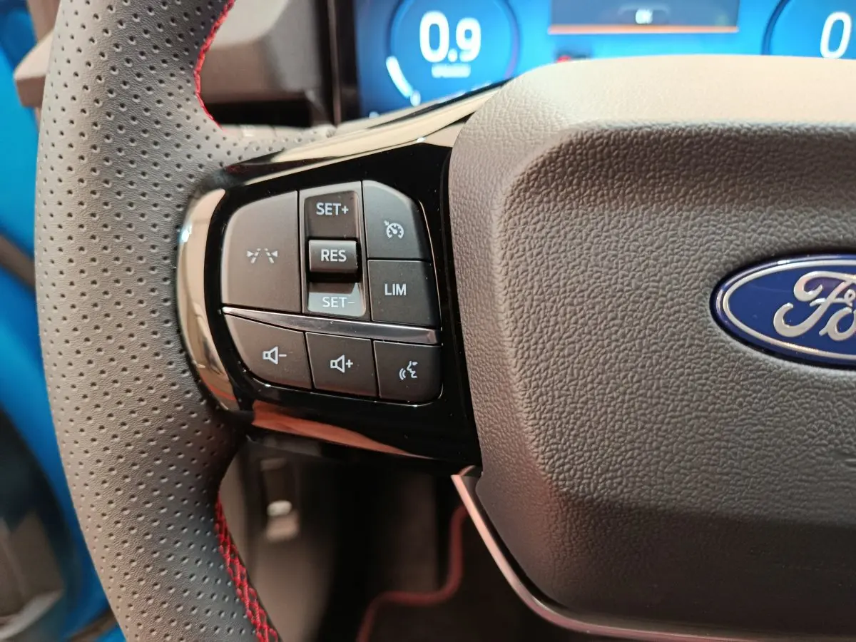 Gros plan sur le volant perforé avec commandes multifonctions du Ford Puma bleu 2025, affichage numérique en arrière-plan.