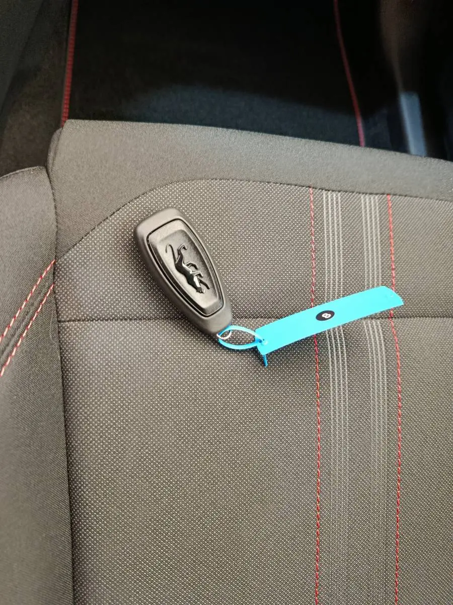 Gros plan sur une clé Ford posée sur un siège tissu gris foncé avec surpiqûres rouges, intérieur du Ford Puma.