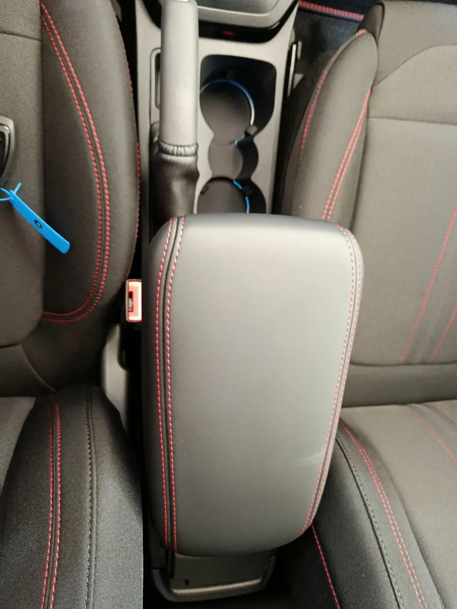 Vue plongeante sur l'accoudoir central noir avec surpiqûres rouges entre les sièges avant du Ford Puma bleu.