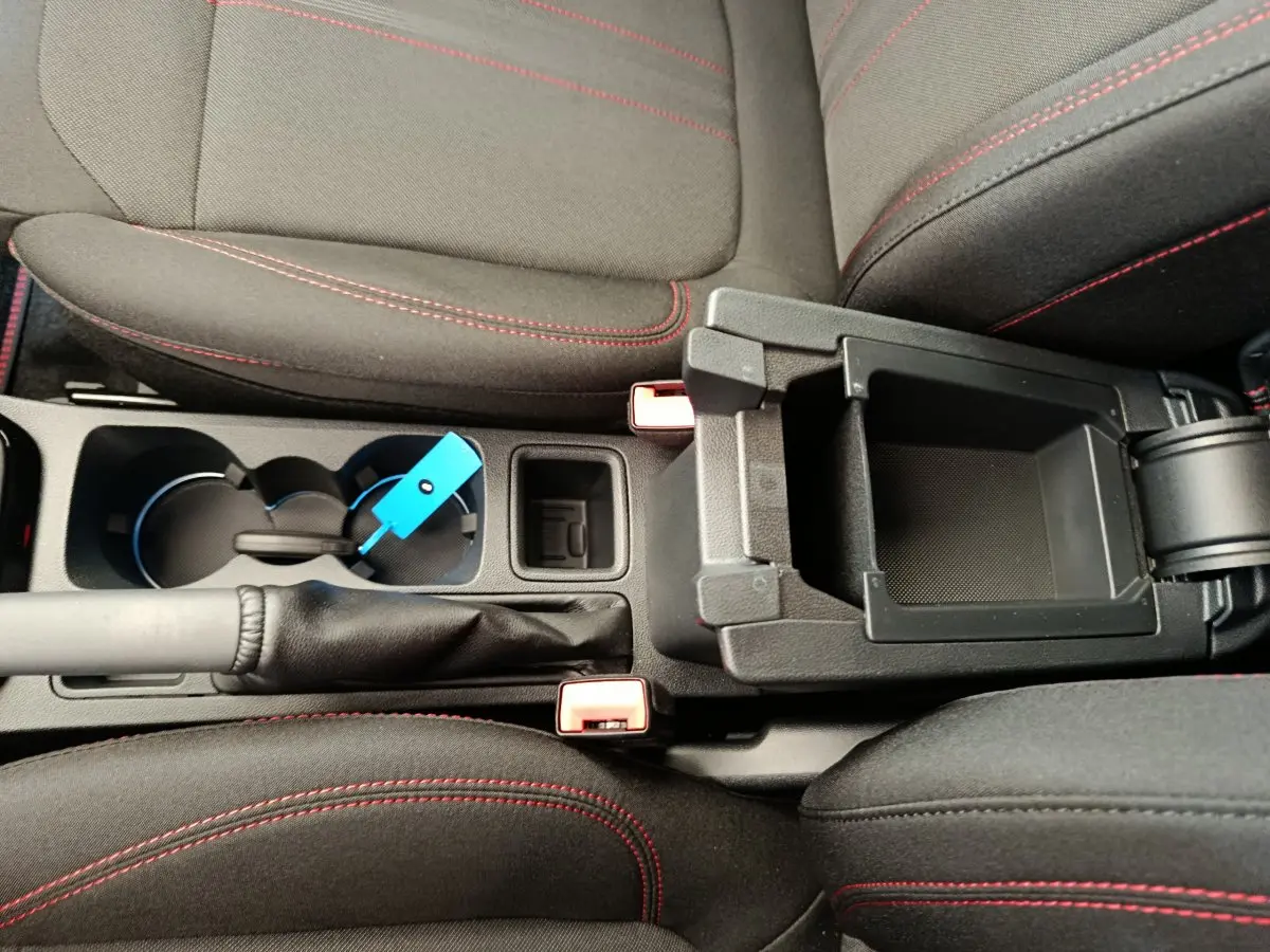 Vue rapprochée de la console centrale du Ford Puma 2025, montrant les sièges noirs avec surpiqûres rouges et un rangement ouvert.