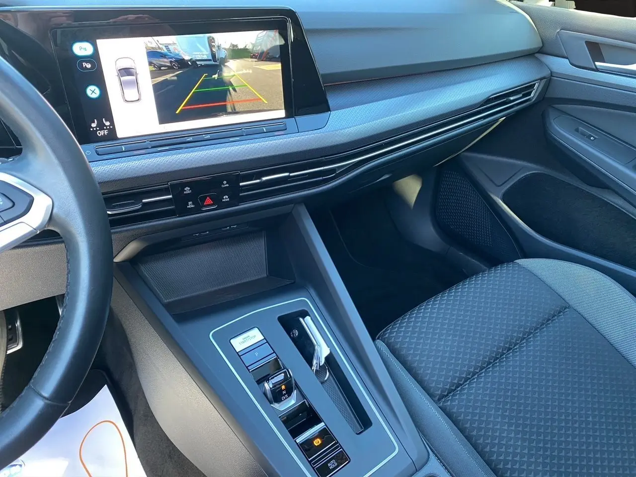 Vue intérieure côté passager de la Volkswagen Golf VIII noire, avec écran tactile affichant la caméra de recul.