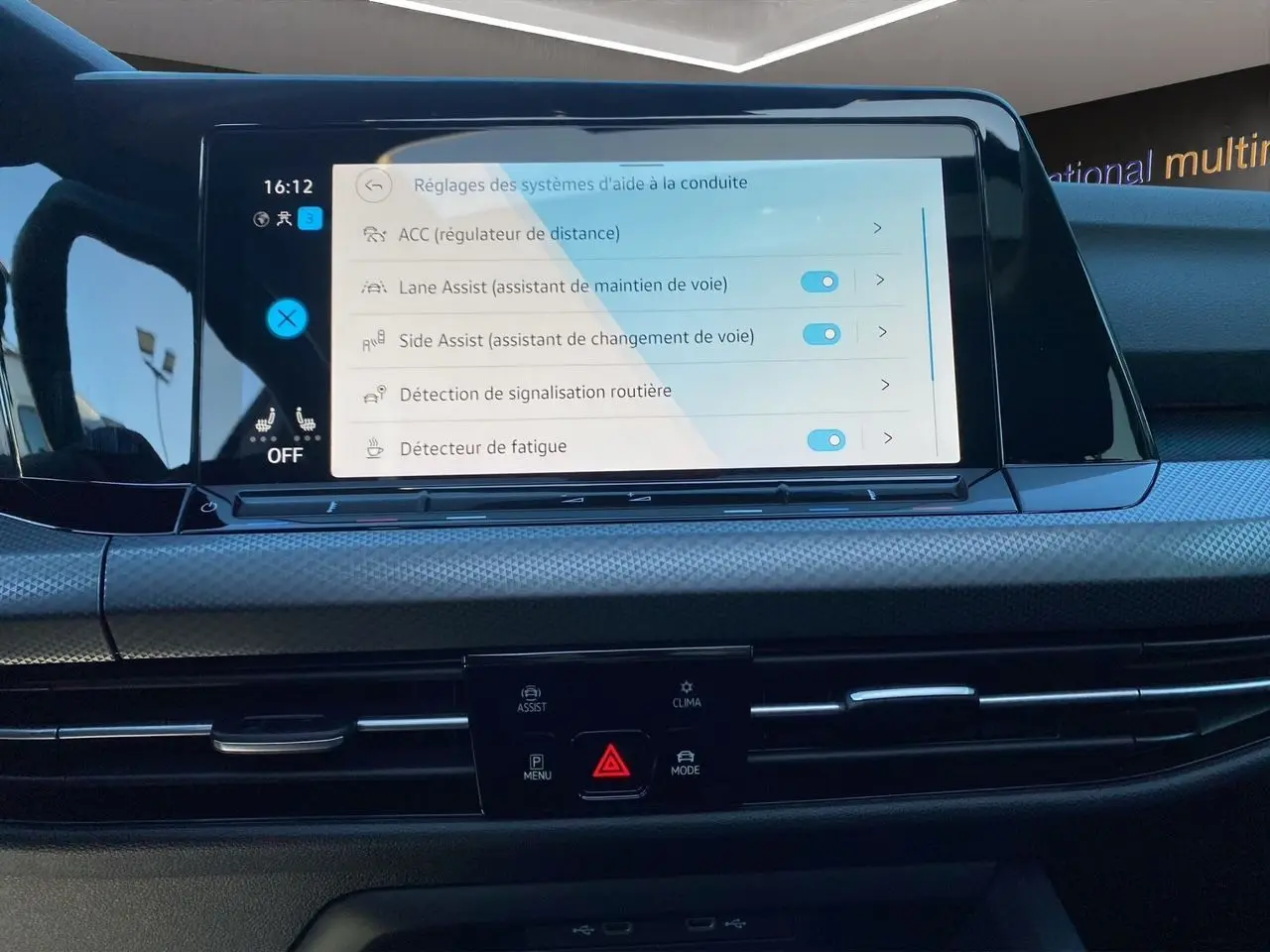 Vue rapprochée de l’écran tactile central de la Volkswagen Golf VIII noire affichant les réglages d’aides à la conduite.