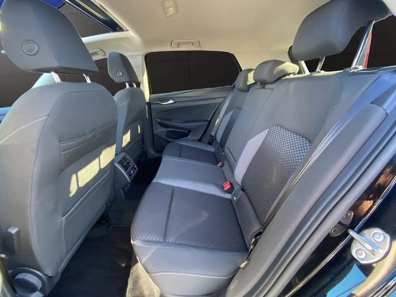 Vue intérieure arrière côté droit de la Volkswagen Golf VIII noire, montrant les sièges arrière en tissu noir et gris.