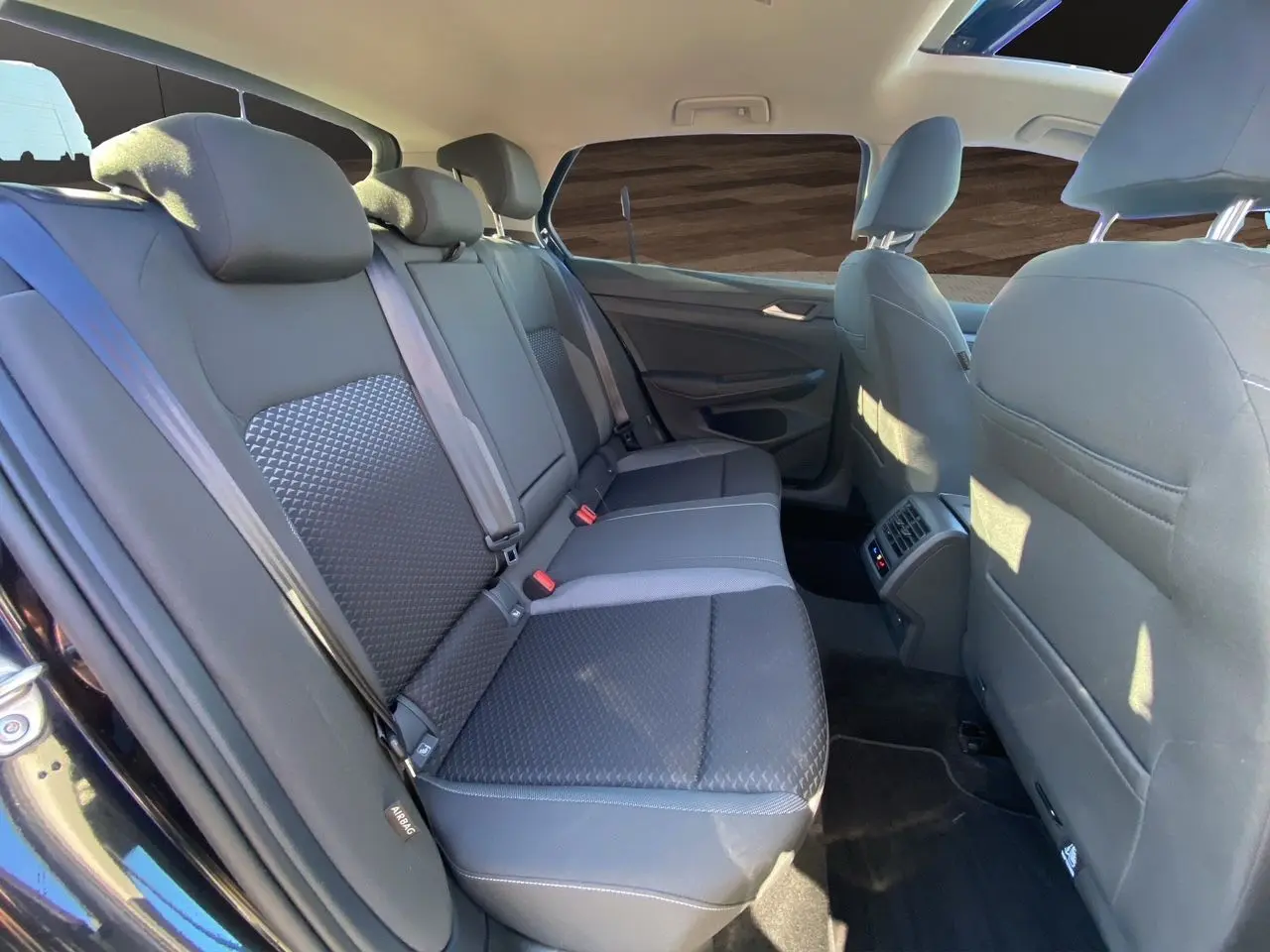 Vue intérieure arrière côté droit de la Volkswagen Golf VIII noire, montrant les sièges arrière et le toit panoramique.