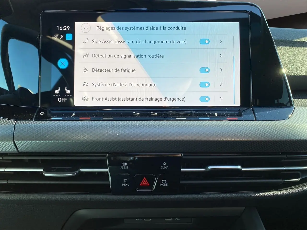 Vue rapprochée de l'écran tactile central de la Volkswagen Golf VIII noire, affichant les réglages d'aide à la conduite.