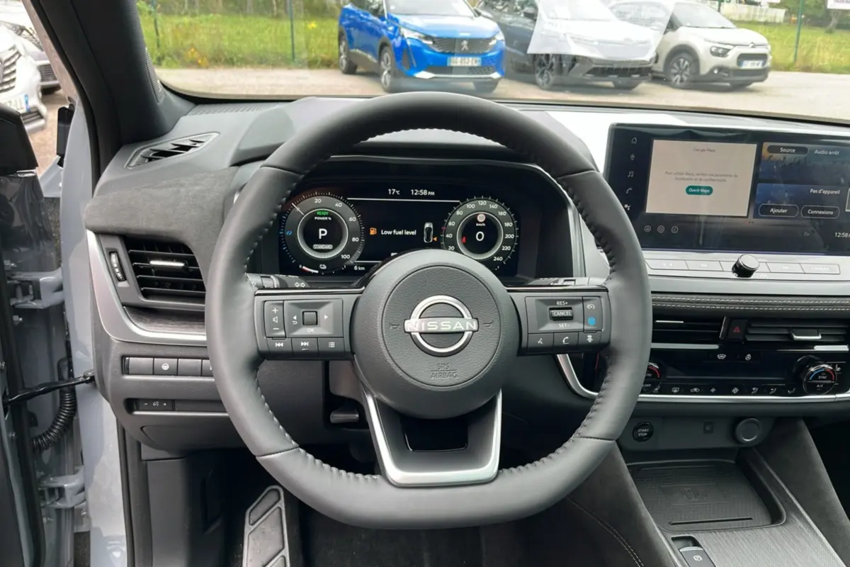Vue intérieure centrée sur le volant cuir du Nissan Qashqai E-POWER 205 Tekna Plus gris argile avec tableau de bord numérique.
