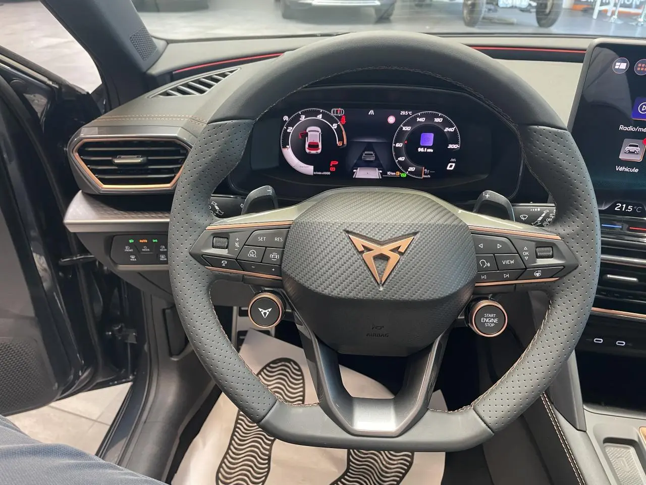 Vue intérieure centrée sur le volant perforé noir avec logo Cupra cuivré et tableau de bord digital du Cupra Leon gris.