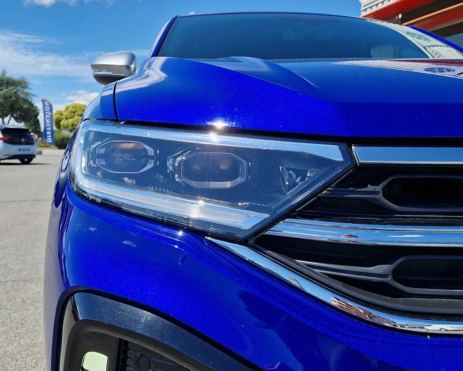 Gros plan sur l'avant gauche du Volkswagen T-Roc bleu Lapiz 2022, mettant en valeur son phare LED et la calandre chromée.