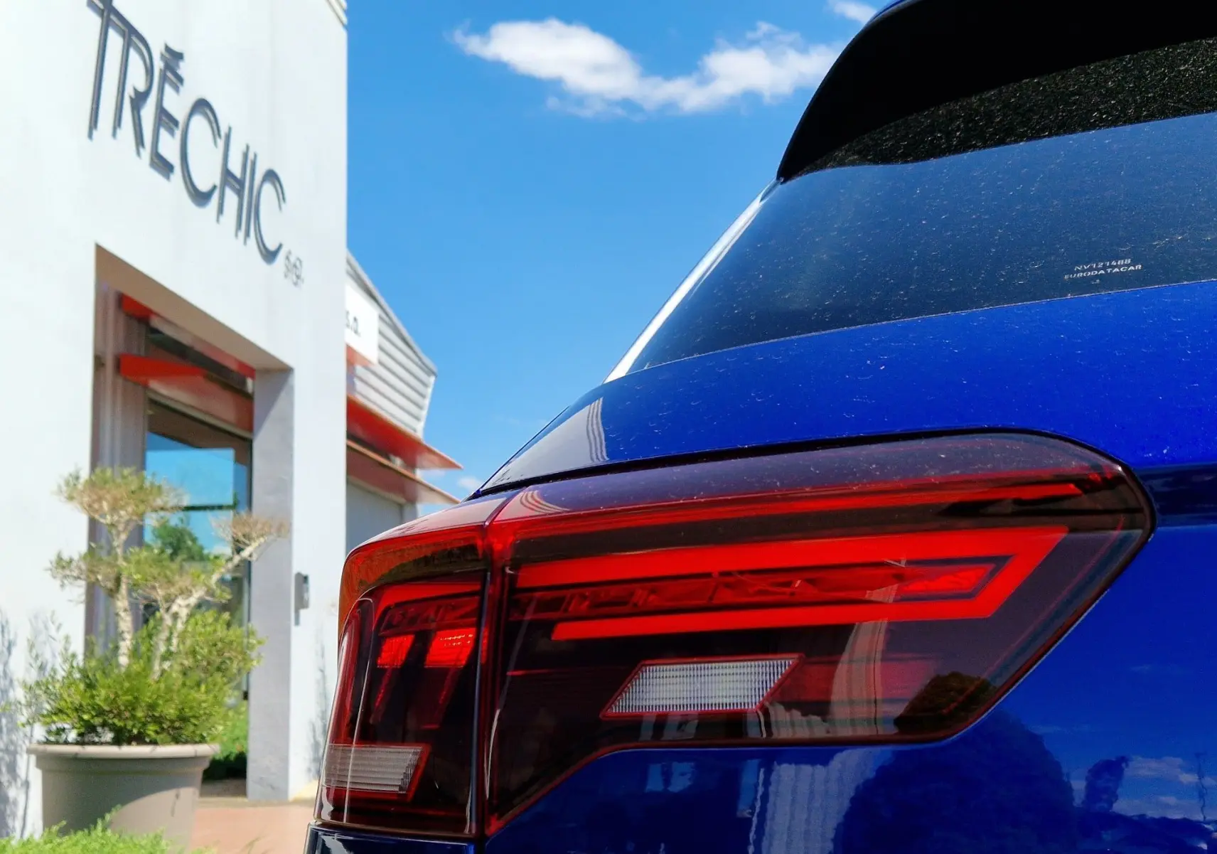 Gros plan sur le feu arrière droit d'un Volkswagen T-Roc bleu Lapiz sous un ciel bleu lumineux.