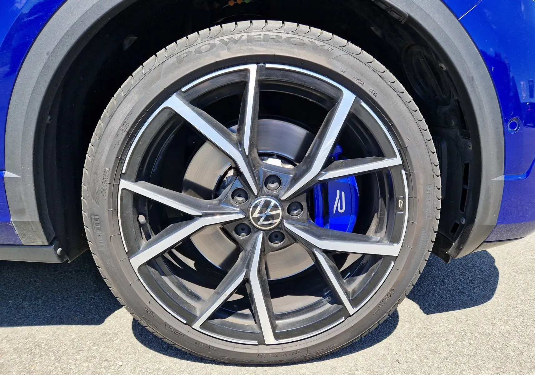 Gros plan sur la jante noire et argentée avec logo VW et étrier de frein bleu du Volkswagen T-Roc bleu Lapiz côté arrière droit.