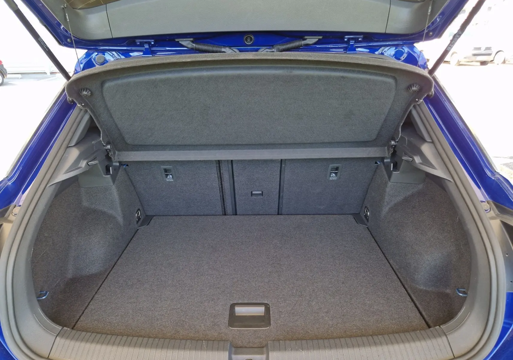 Coffre ouvert du Volkswagen T-Roc bleu Lapiz, vue de l'arrière montrant un espace de chargement propre et spacieux.