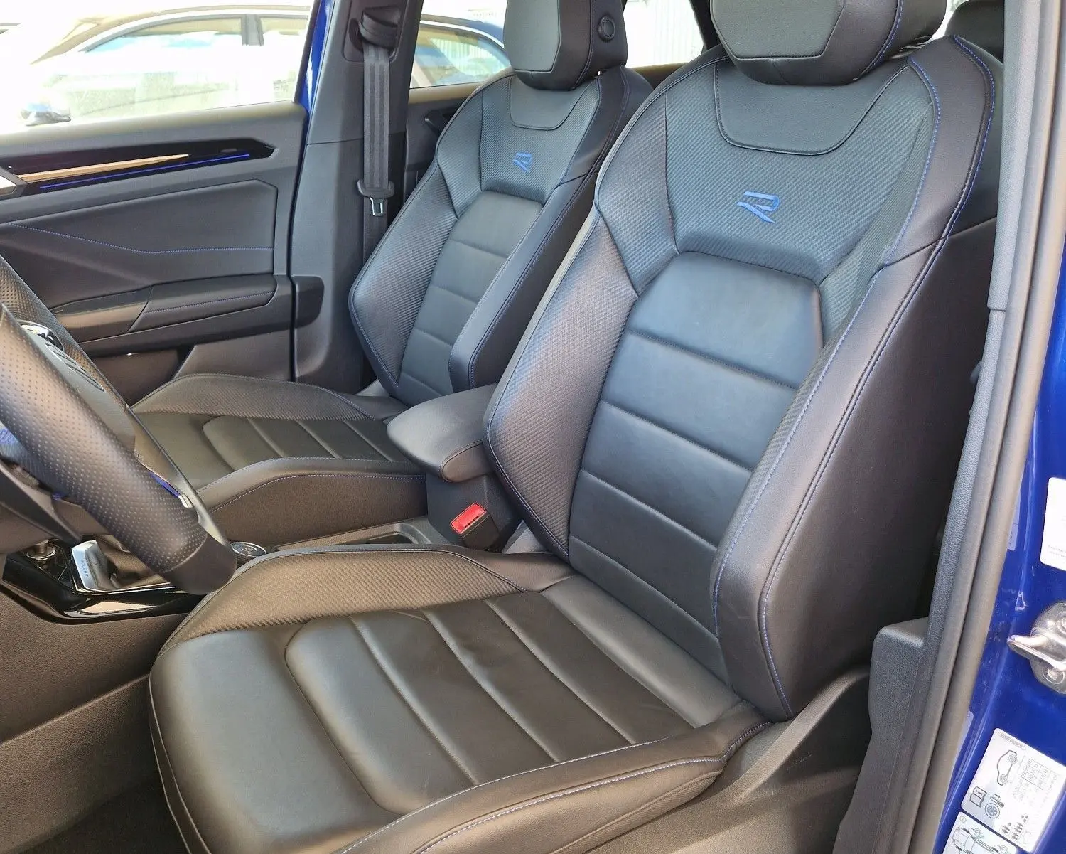 Vue intérieure côté conducteur du Volkswagen T-Roc bleu Lapiz 2022, sièges cuir noirs avec surpiqûres bleues et logo R brodé.