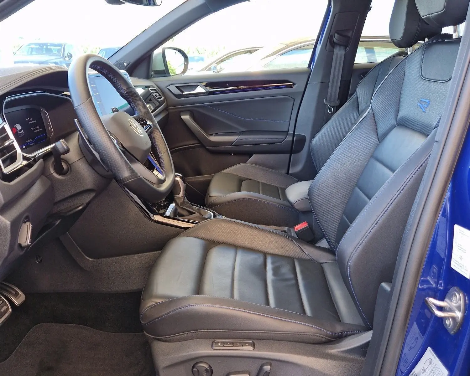 Vue intérieure côté conducteur du Volkswagen T-Roc bleu Lapiz 2022 avec sièges cuir et volant multifonction.