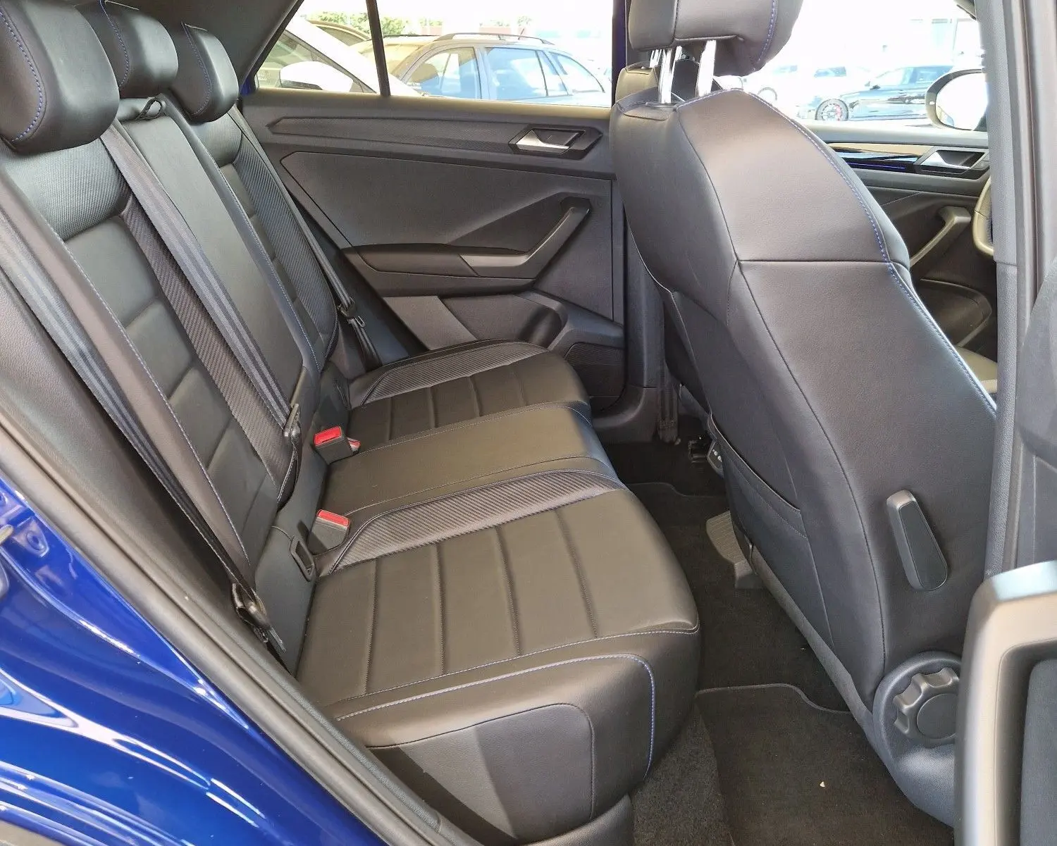 Vue intérieure côté gauche du Volkswagen T-Roc bleu Lapiz, montrant les sièges arrière en cuir noir avec surpiqûres bleues.