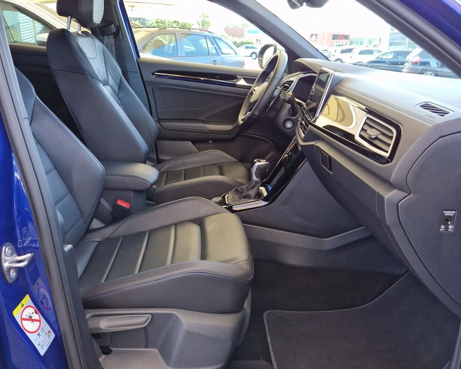 Intérieur du Volkswagen T-Roc bleu Lapiz 2022, vue côté gauche montrant les sièges en cuir et le tableau de bord moderne.