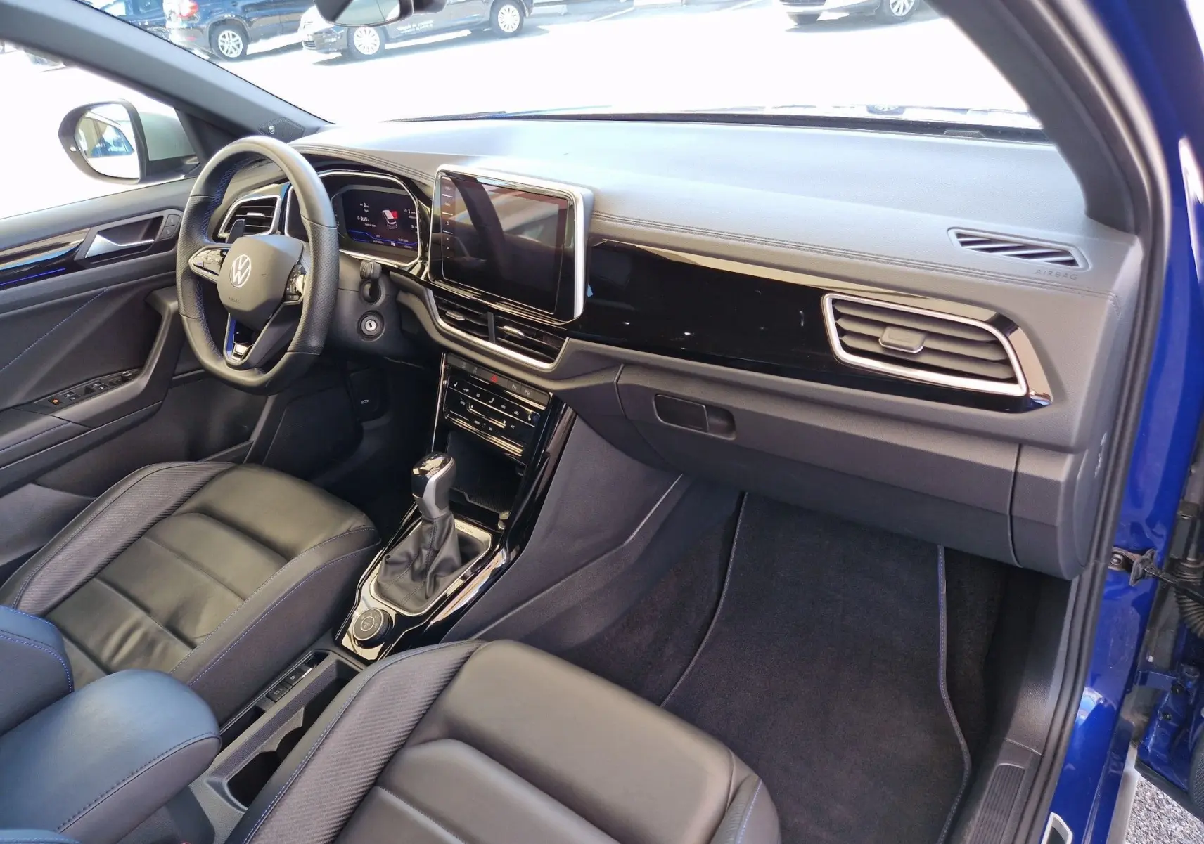 Vue intérieure côté conducteur du Volkswagen T-Roc bleu Lapiz 2022, avec tableau de bord moderne et sièges cuir noirs.