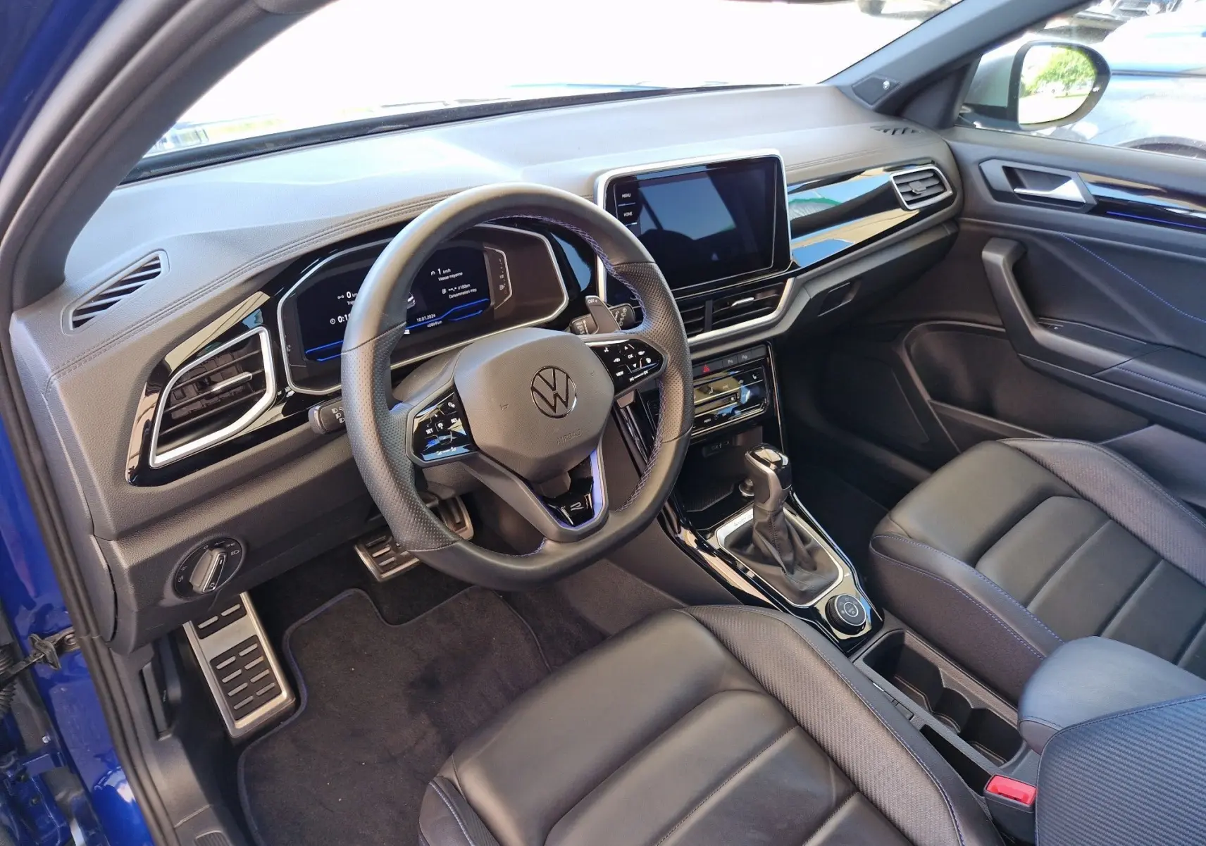 Intérieur du Volkswagen T-Roc bleu Lapiz 2022, vue côté conducteur montrant tableau de bord numérique et sièges cuir noirs.