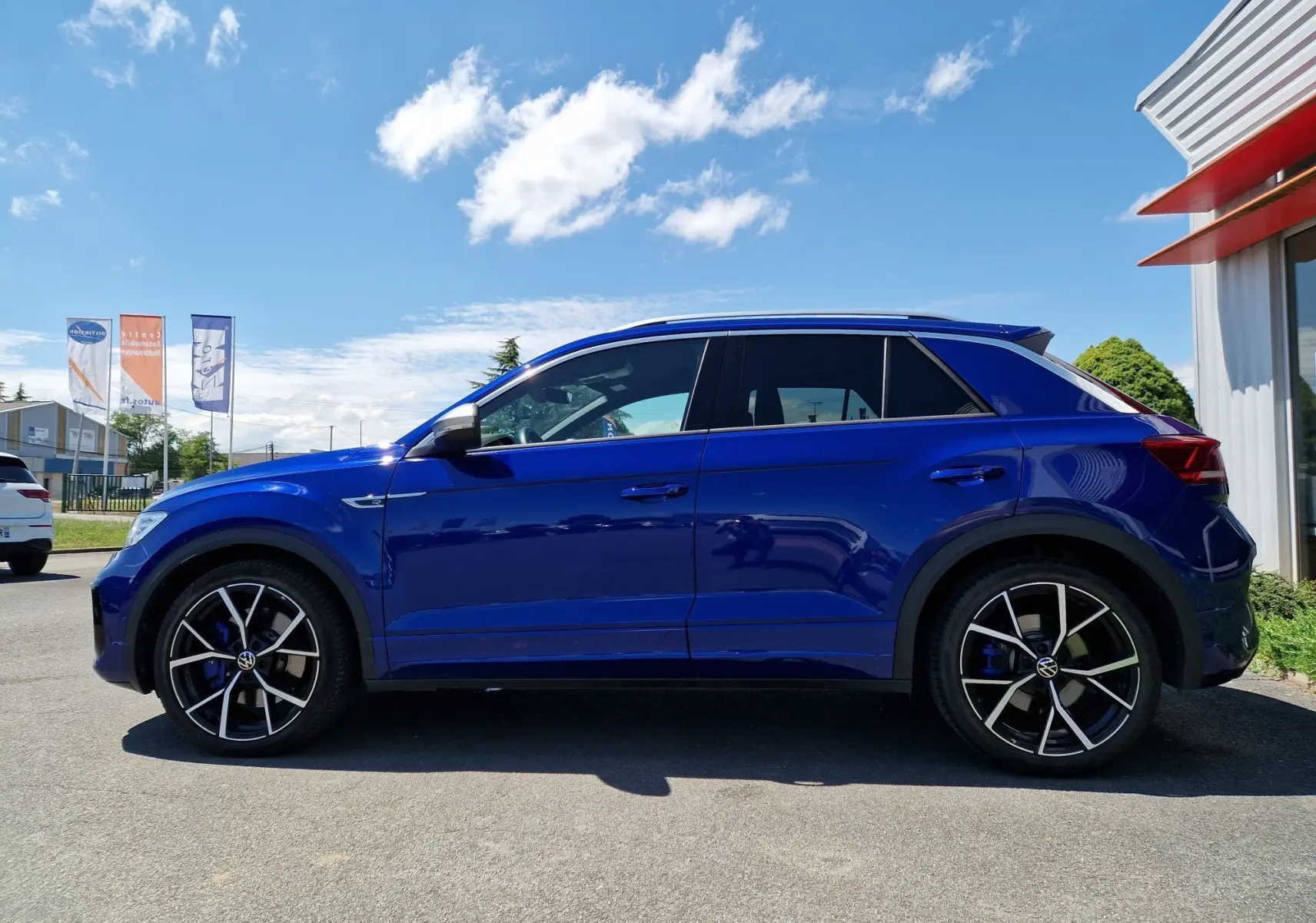 Profil latéral droit d'un Volkswagen T-Roc bleu Lapiz avec jantes alliage noires et détails bleus sur fond urbain.