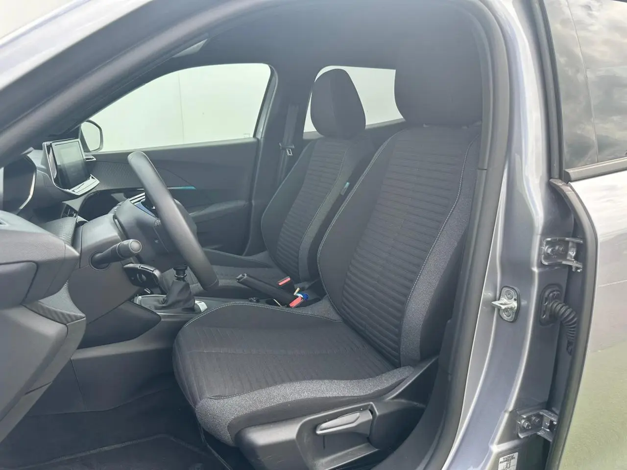 Intérieur avant de la Peugeot 2008 gris clair 2022, sièges tissu noir, volant compact et écran tactile visible côté conducteur.