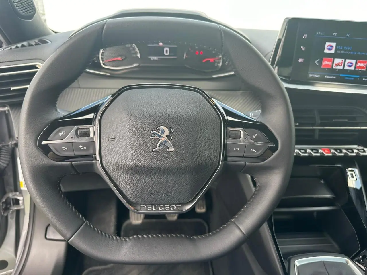 Volant compact en cuir noir avec logo Peugeot, tableau de bord numérique et écran tactile central du Peugeot 2008 gris clair.