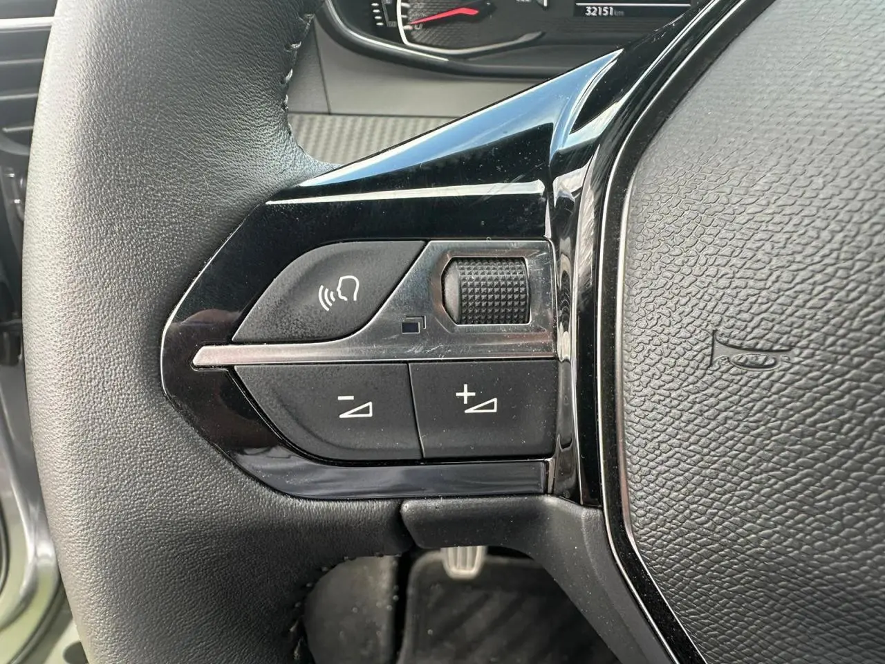 Gros plan sur les commandes multimédia à gauche du volant noir du Peugeot 2008 gris clair de 2022.