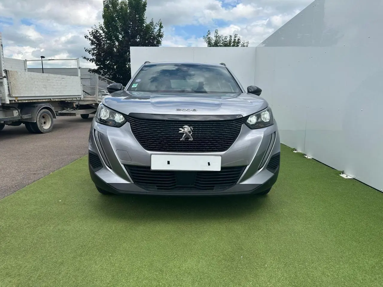 Peugeot 2008 gris clair vue de face, avec calandre noire et logo lion central bien visible.
