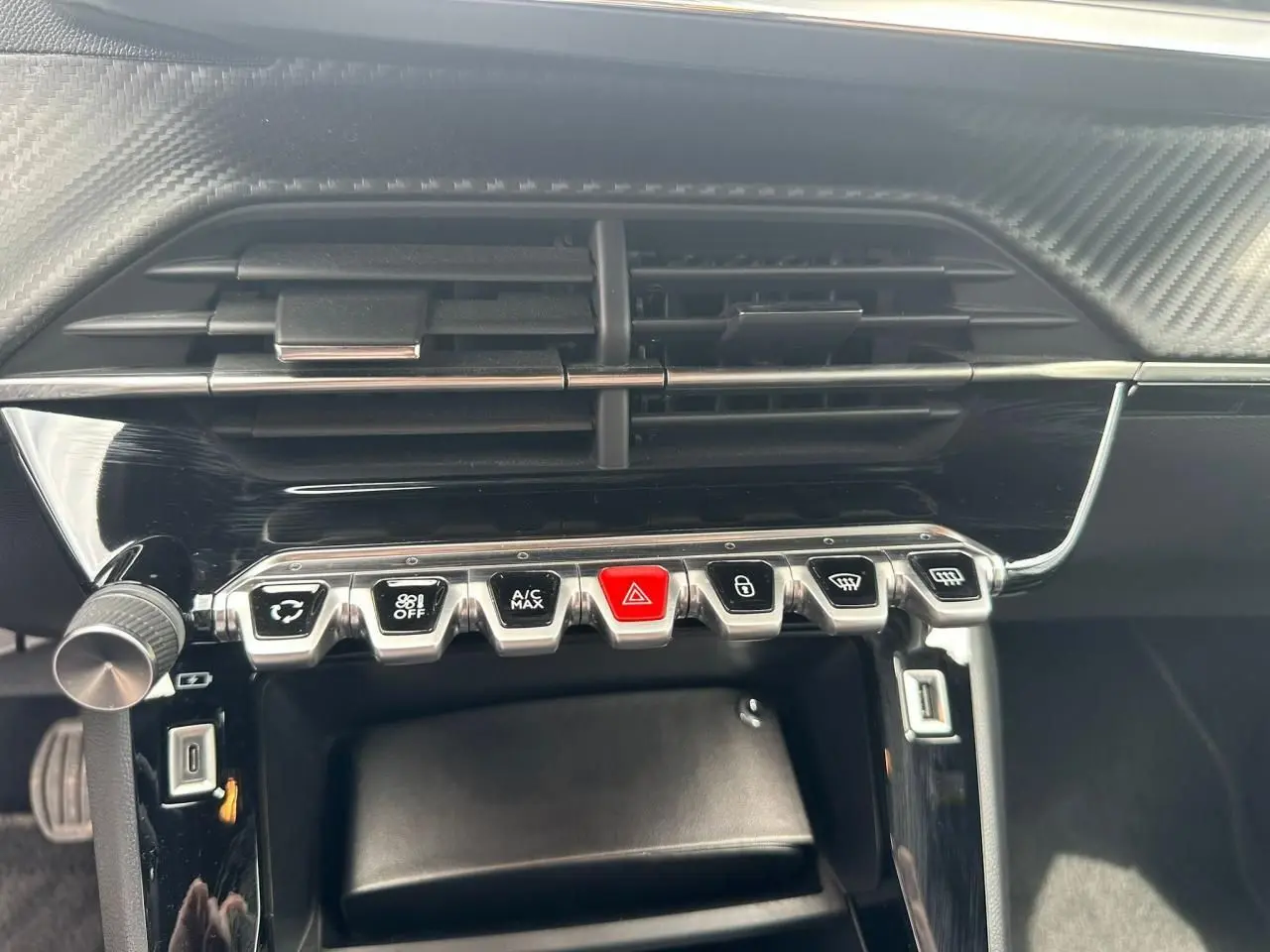 Gros plan sur la console centrale noire du Peugeot 2008 II avec boutons argentés et rouge d'alerte, prise USB visible.